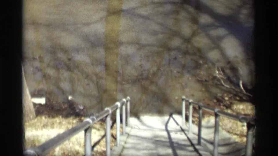 1969 Savage, Minnesota 8mm frame showing a concrete walkway and metal railings descending through leafless winter woods.
