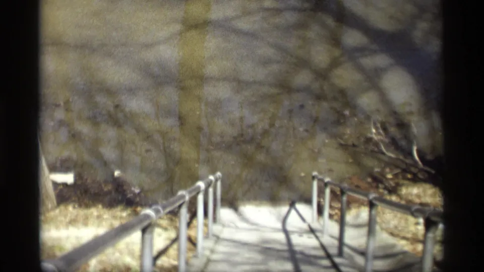 Vintage 8mm view from Savage, Minnesota in 1969, looking along a railed walkway into shadowed winter woods.