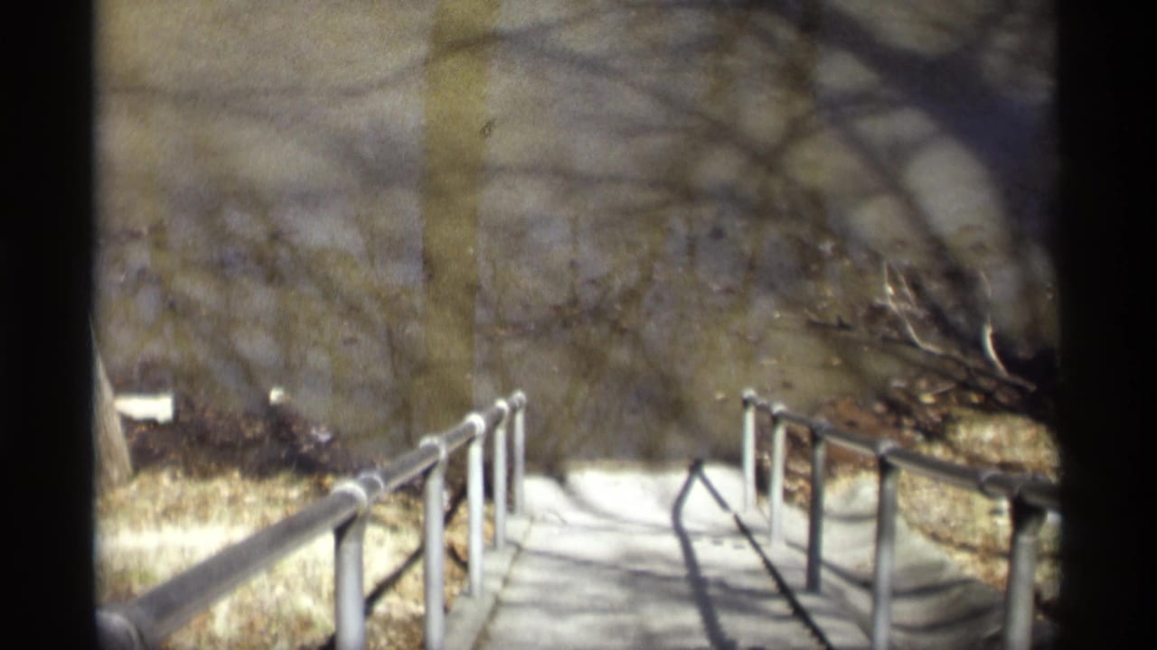 1969 8mm view in Savage, Minnesota, looking down a concrete park path bordered by metal railings and bare trees.
