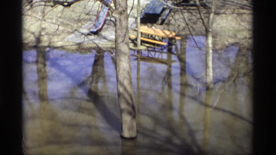 Flooded Savage, Minnesota park in 1969, with a slide, picnic table, tree trunks, reflections, and murky water.