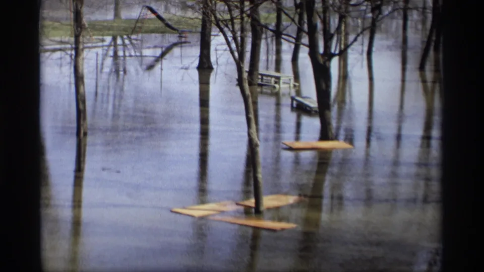 Savage, Minnesota flood scene from 1969, showing still water around bare trees, floating boards, and a picnic table near the far bank.
