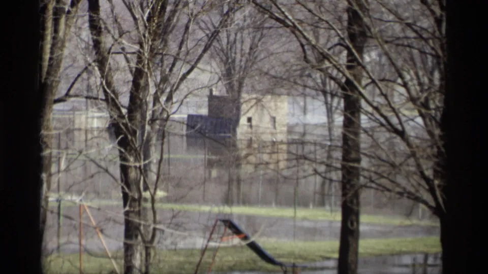 1969 Savage, Minnesota park flooding with bare trees in the foreground, standing water, playground equipment, grass, and a distant brick building.