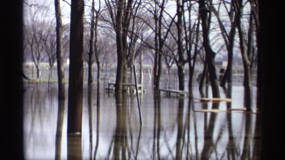 1969 Savage, Minnesota 8mm frame showing bare trees reflected in floodwater with partially submerged park tables beyond.