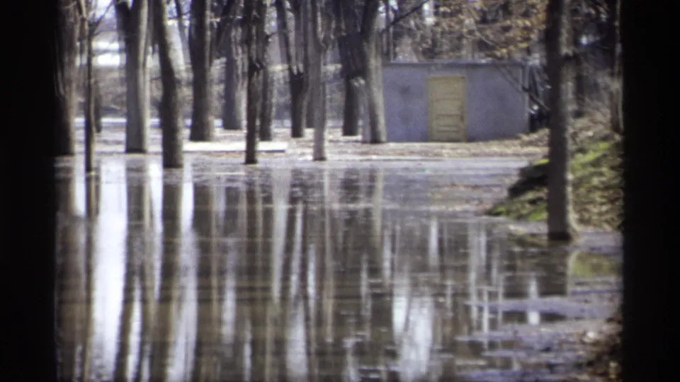 1969 Savage, Minnesota 8mm frame showing a small concrete building behind trees standing in reflective floodwater.