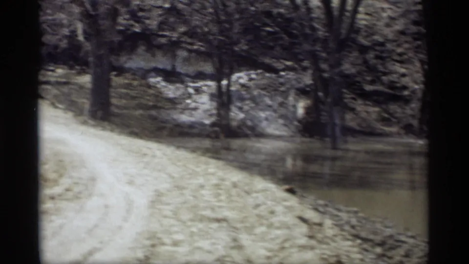 1969 Savage, Minnesota frame showing a dirt road beside floodwater and trees, with soft home-movie grain and visible film borders.