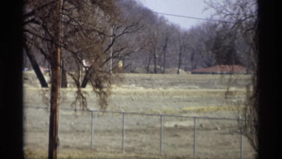 Savage, Minnesota home-movie frame from 1969 showing a chain-link fence, winter-bare trees, utility pole, overhead wire, and wooded background.