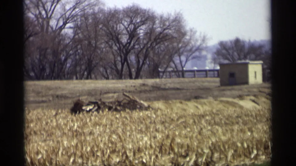 1969 Savage, Minnesota landscape showing dry field growth, leafless trees, a distant rail or fence, and a small beige utility building.