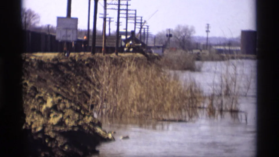 1969 Savage, Minnesota view of floodwater, reeds, muddy ground, and utility poles along a distant road or rail corridor.