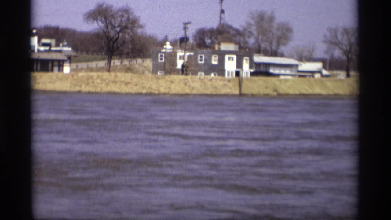 1969 8mm view in Savage, Minnesota, showing rippling river water and houses behind a grassy embankment.