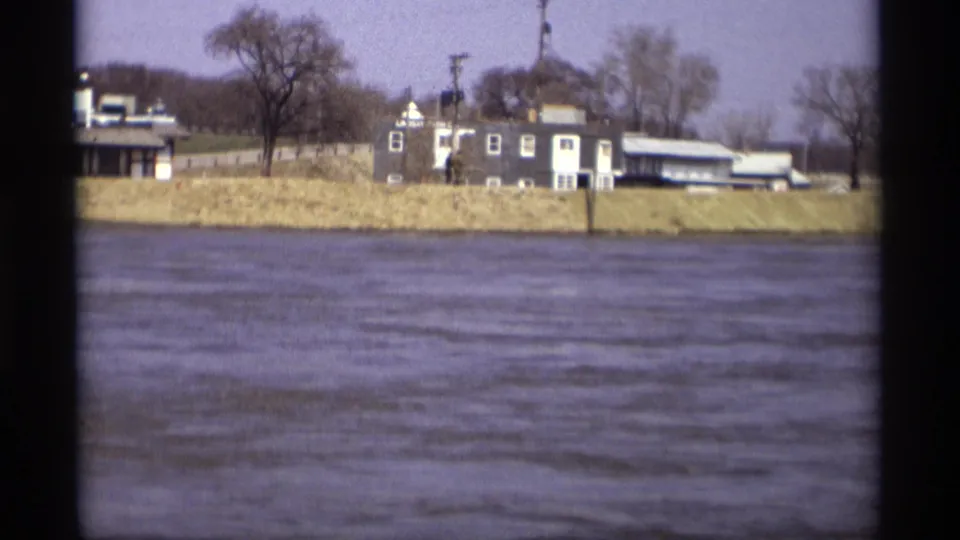 1969 8mm view in Savage, Minnesota, showing rippling river water and houses behind a grassy embankment.