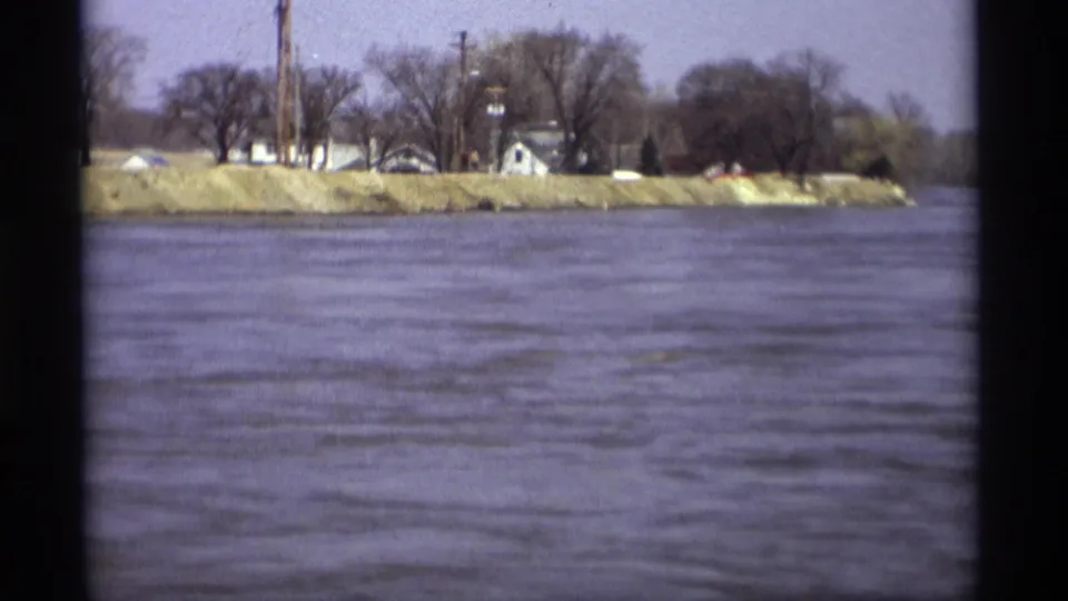 Savage, Minnesota river view with houses and trees across the water; a small red element near the bank may be a distant person or object.