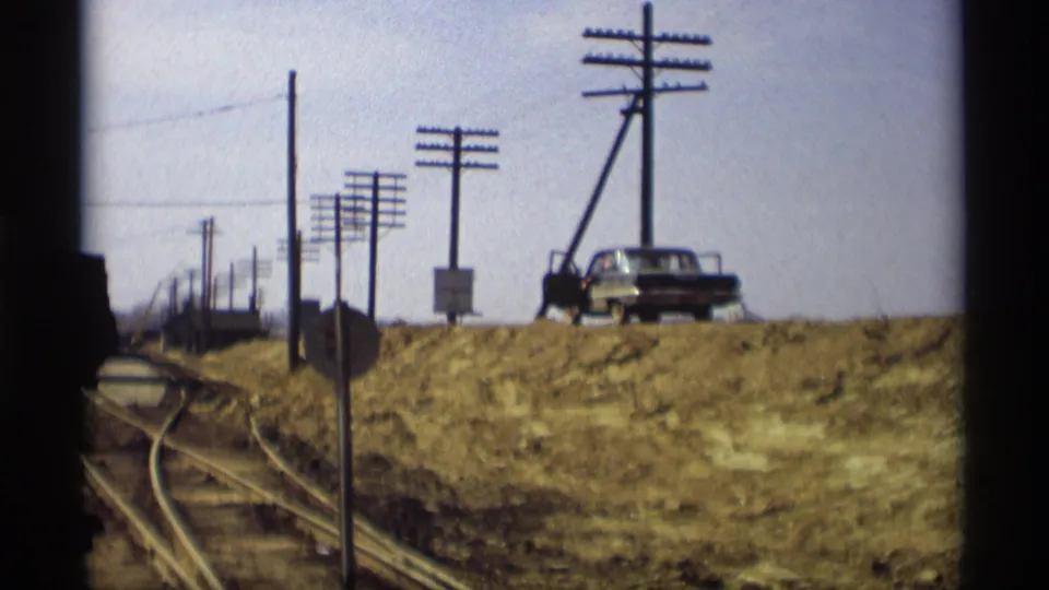 A wider 1969 Savage, Minnesota view shows rail tracks, utility poles, a dirt embankment, and a parked mid-century vehicle near the work area.