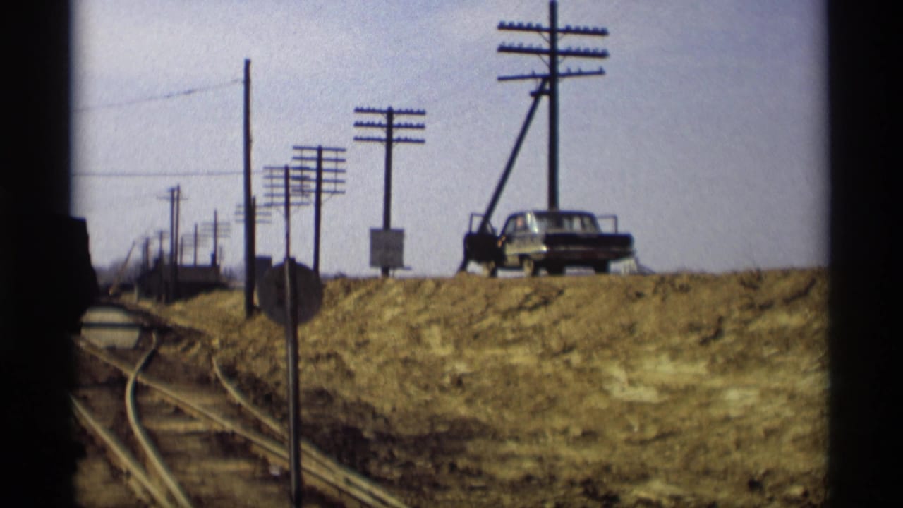 Roadside view with utility poles, tracks, and a parked car near flooded ground.