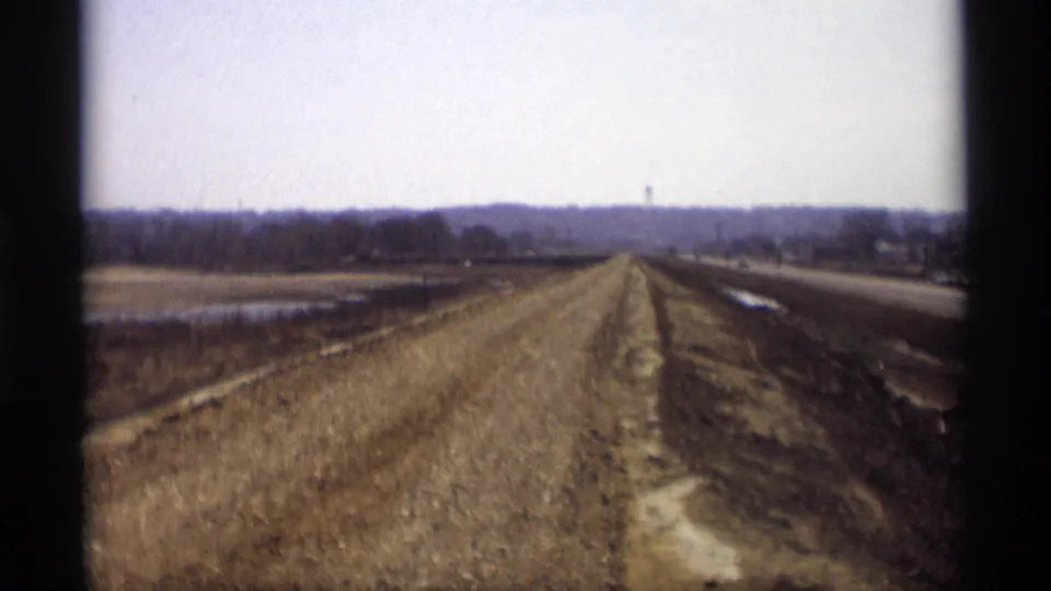 A soft 8mm view of the new roadbed in Savage, Minnesota, with muddy drainage areas, fields, and a highway running alongside it.