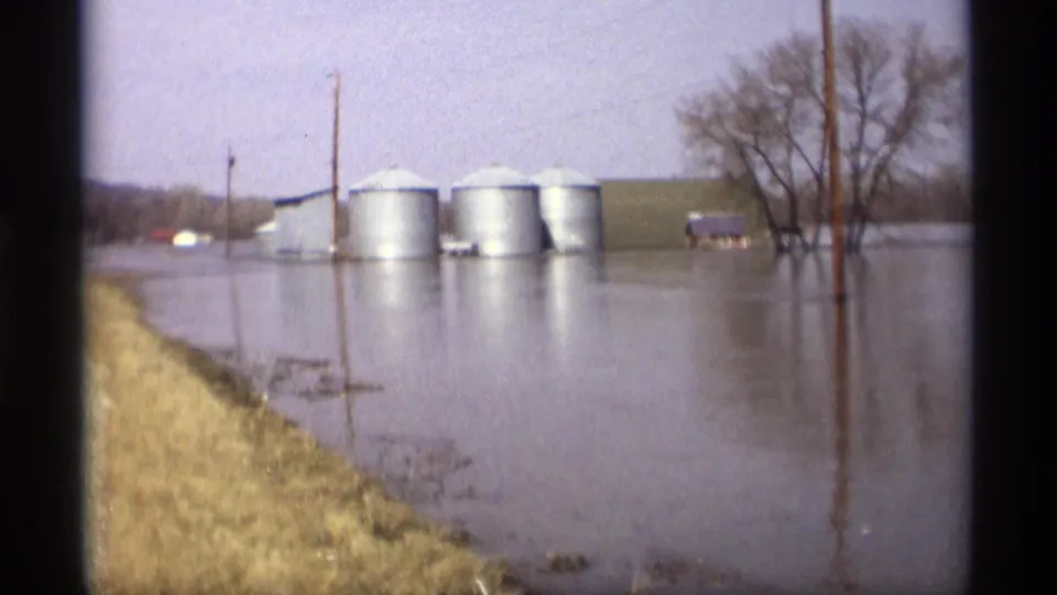 A nearby rural property area in Savage, Minnesota, appears partly flooded, with metal grain bins, utility poles, and leafless trees visible.