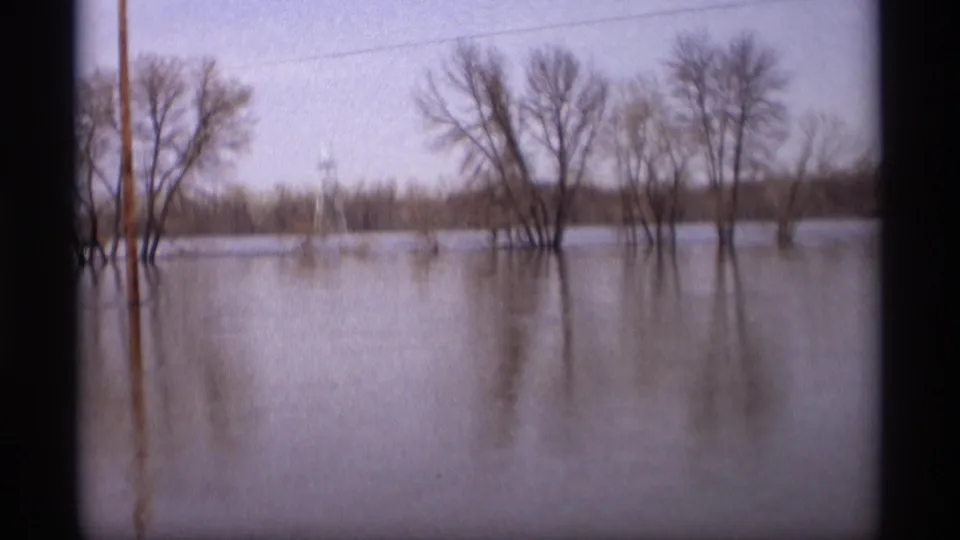 1969 Savage, Minnesota frame looking across floodwater toward bare trees, utility poles, and a distant wooded edge.