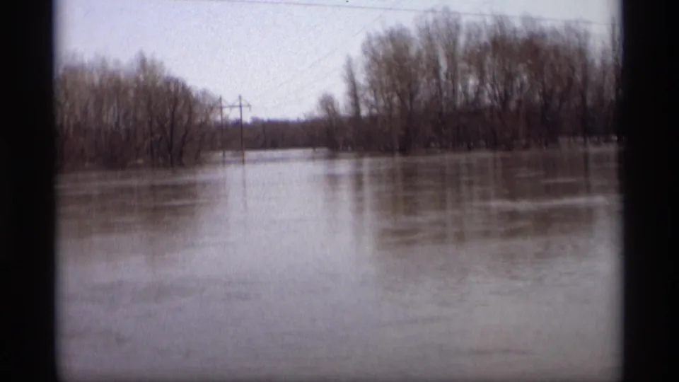 Savage, Minnesota flood scene on 8mm film, with high water surrounding bare trees and utility poles in a rural area.