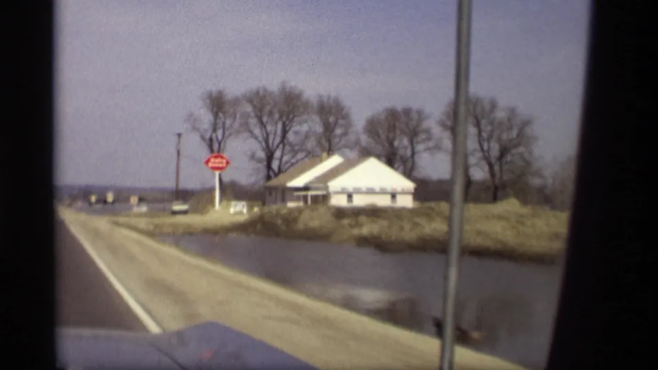 1969 Savage, Minnesota windshield view of a stop sign and white roadside building surrounded by waterlogged land.
