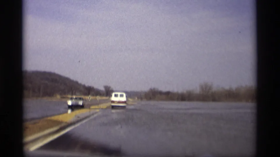 1969 Savage, Minnesota frame showing vehicles navigating a road bordered by broad standing floodwater.