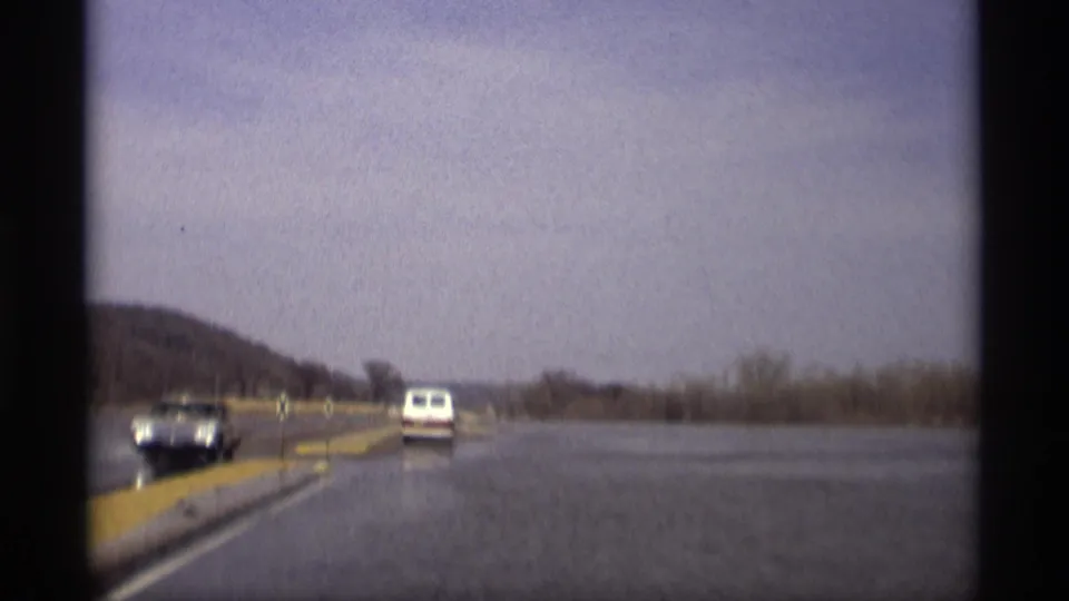 1969 Savage, Minnesota home-movie frame with a white van ahead and floodwater spread across both sides of the road.