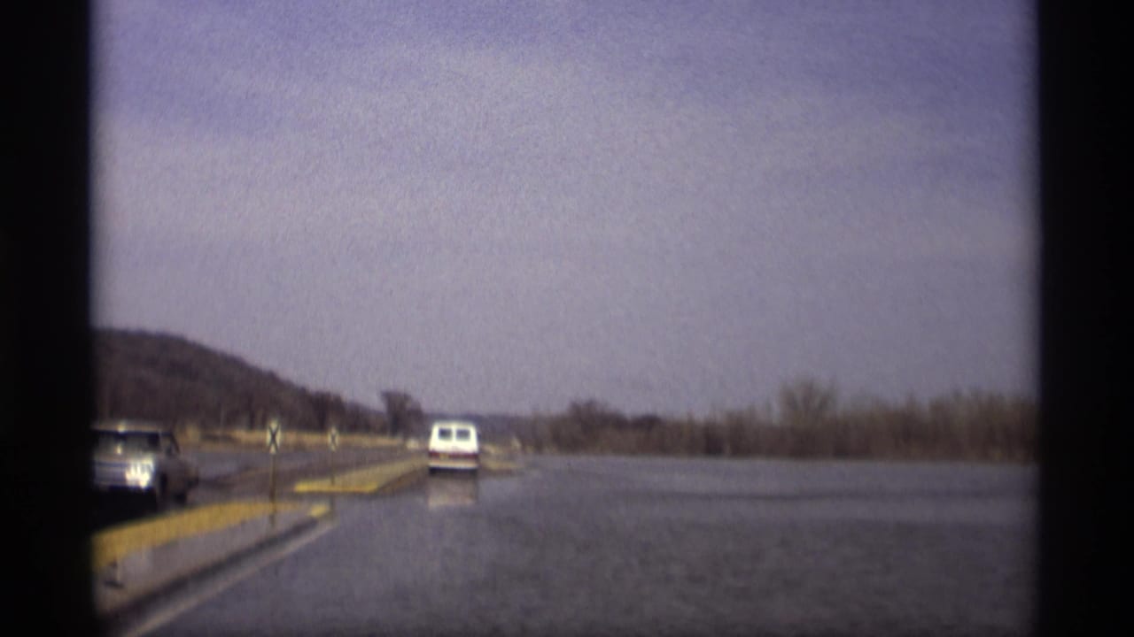 Vehicle view of a flooded roadway with a white van ahead and a car approaching.