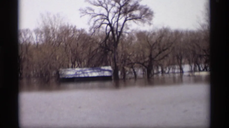 1969 Savage, Minnesota flood scene with a small shed, bare trees, and standing water across a rural low area.
