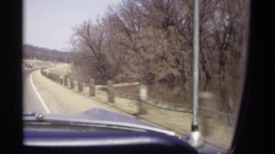 1969 Savage, Minnesota home-movie view from inside a moving car along a curving rural road with bare trees and roadside posts.