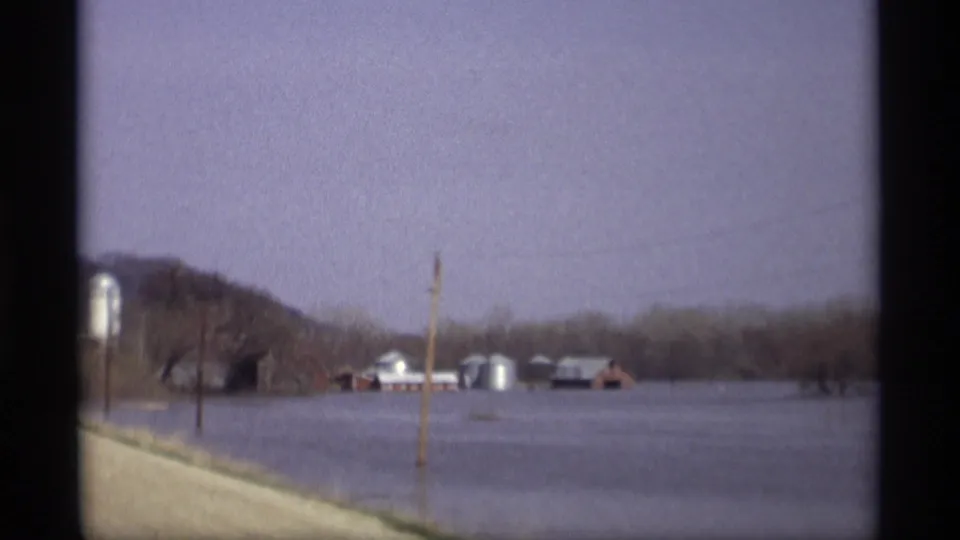 1969 Savage, Minnesota roadside view of floodwater surrounding a farmstead with silos, barns, bare trees, and a utility pole.