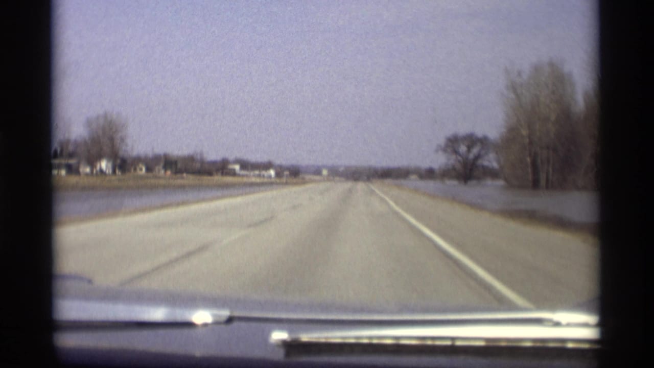 Empty highway viewed over a car dashboard with floodwater along both sides.