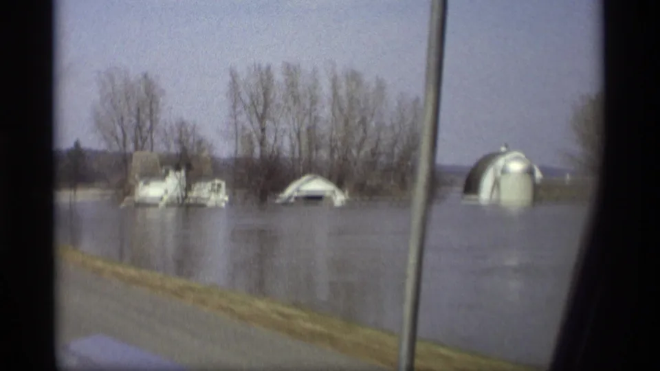 1969 Savage, Minnesota frame with a white house, arched outbuilding, bare trees, and still floodwater beyond the road.