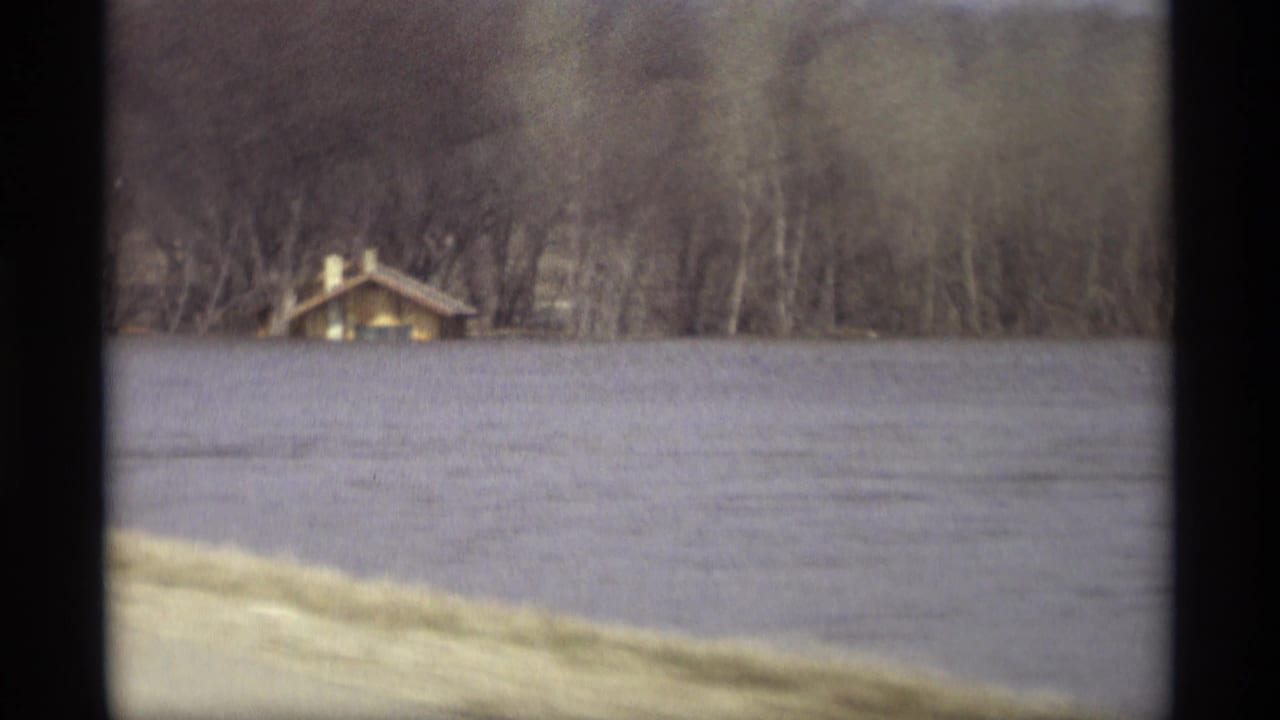 1969 Savage, Minnesota 8mm frame showing floodwater across a rural bank with a small building backed by leafless trees.