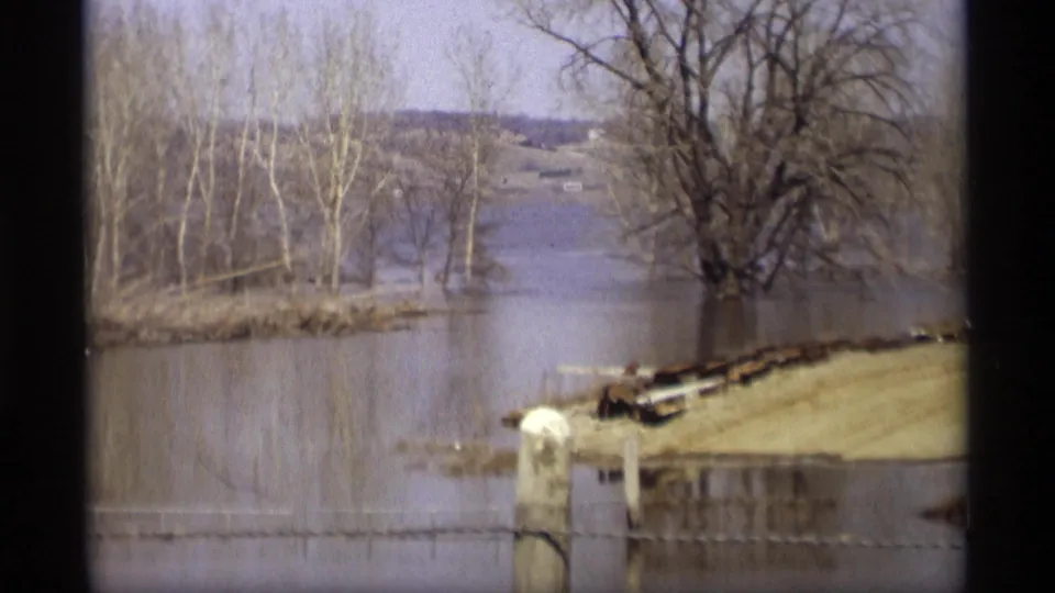 1969 Savage, Minnesota view of floodwater covering the river edge, with bare trees, a fence line, and distant terrain beyond the water.