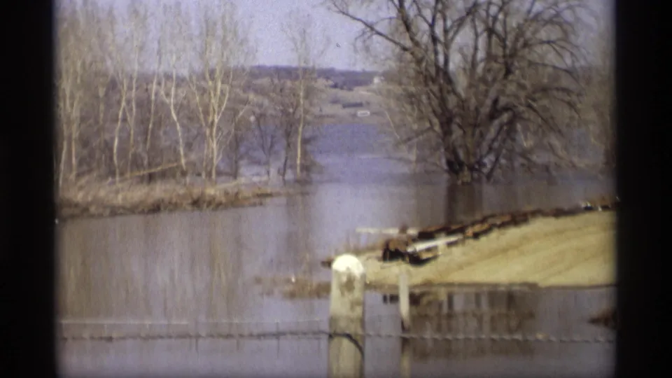 1969 Savage, Minnesota frame of a flooded riverbank where water reaches posts and a low structure beside leafless trees.