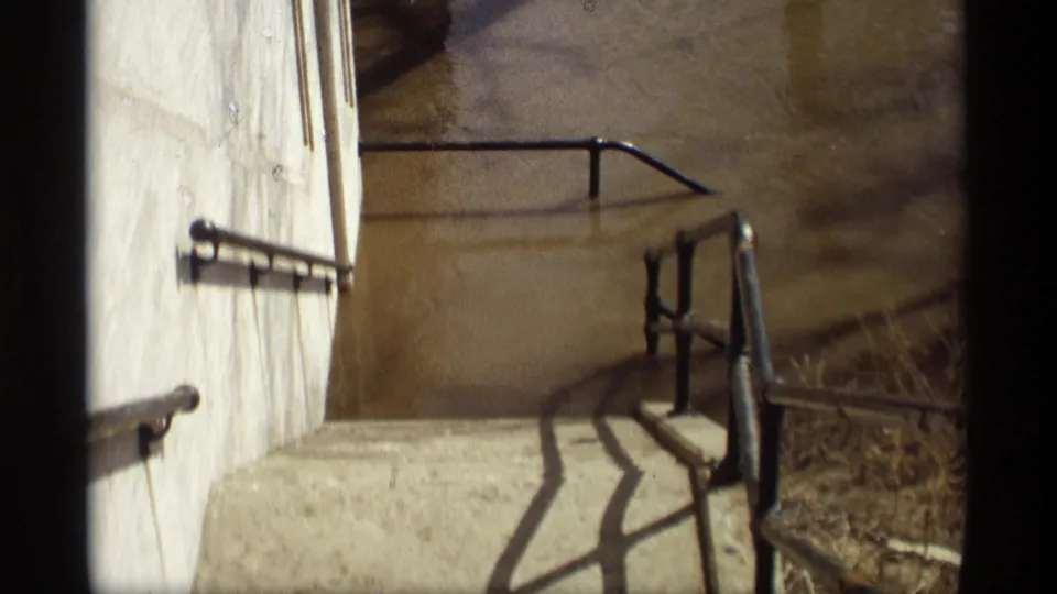 1969 Savage, Minnesota home-movie frame showing a concrete stairwell and railings overlooking murky brown floodwater.