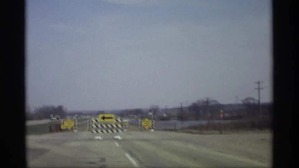 1969 8mm frame from Savage, Minnesota showing a blocked road with yellow signs and floodwater along the roadside.