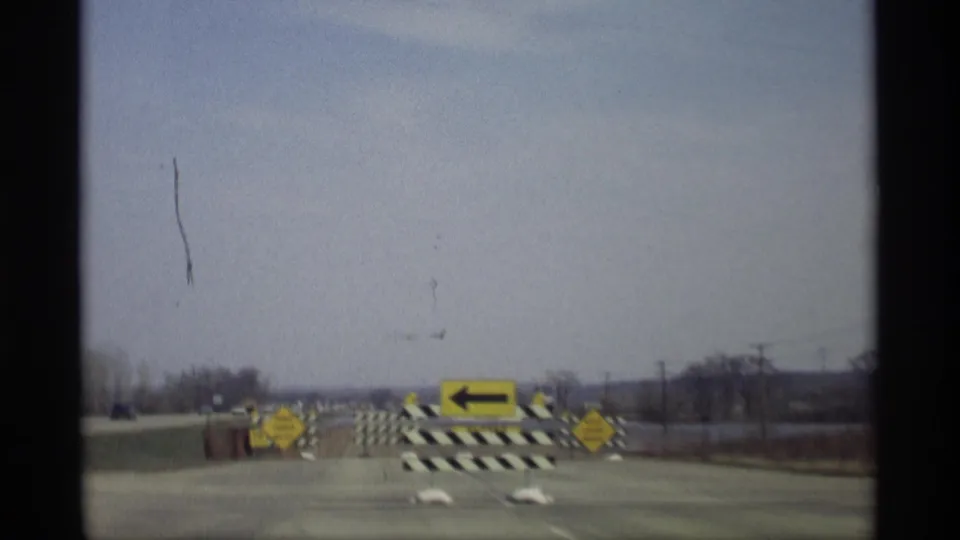 Savage, Minnesota road closure frame with a large yellow left arrow, striped barricades, and floodwater beyond the pavement.