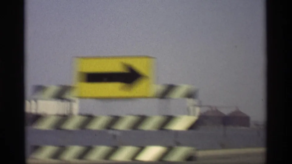 Close moving 8mm view near Savage, Minnesota, of a yellow right-arrow traffic sign with striped roadside barriers, blurred by vehicle motion.