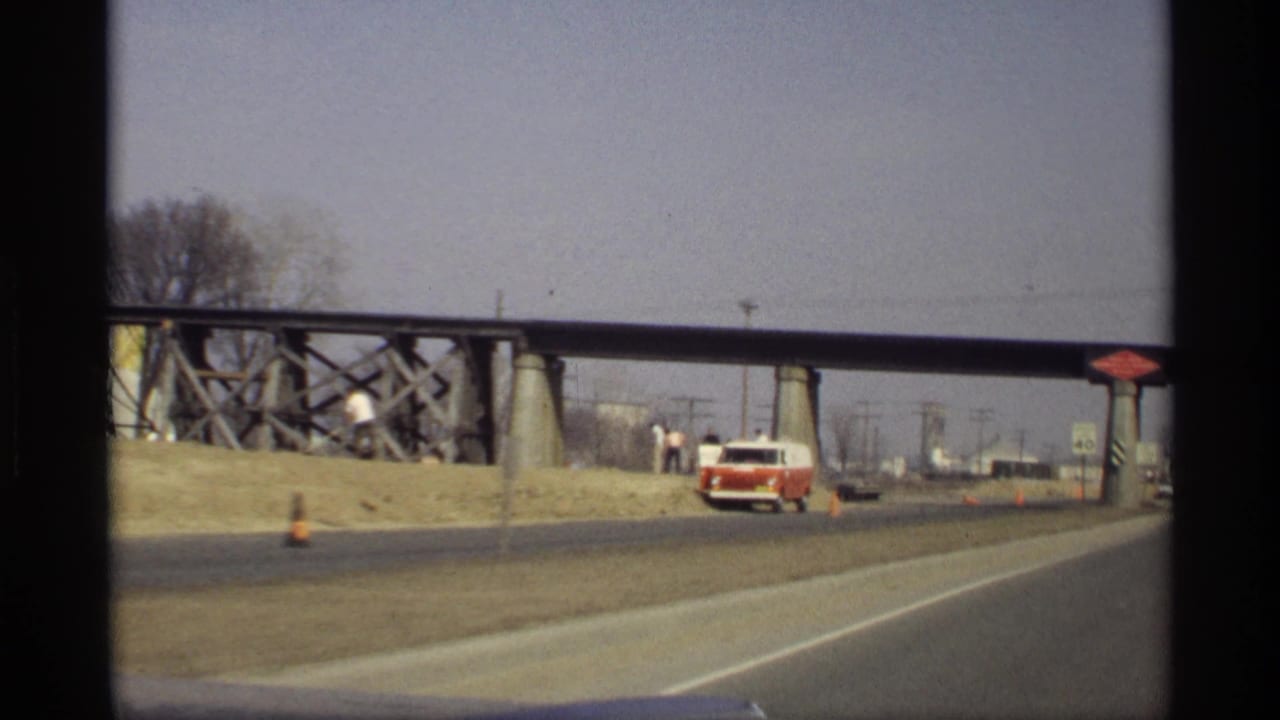 1969 Savage, Minnesota road view from a moving car, showing a red and white van near the shoulder beneath a steel bridge.