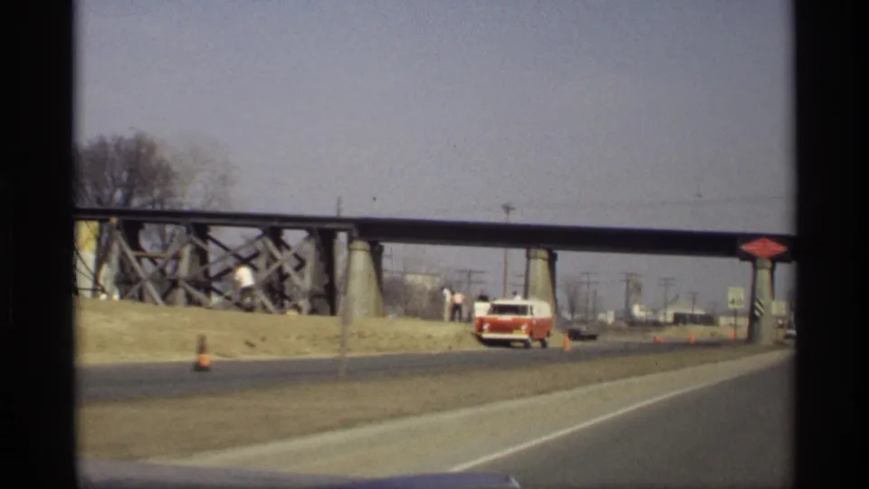 1969 Savage, Minnesota road view from a moving car, showing a red and white van near the shoulder beneath a steel bridge.