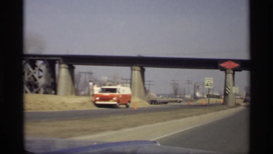 Moving-car view of a red and white van pulled near the roadside under a bridge in Savage, Minnesota, with traffic cones visible.
