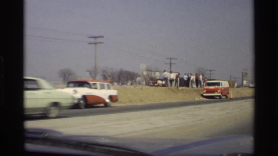 1969 roadside scene in Savage, Minnesota, with a classic sedan passing and a small group of people gathered near the shoulder.