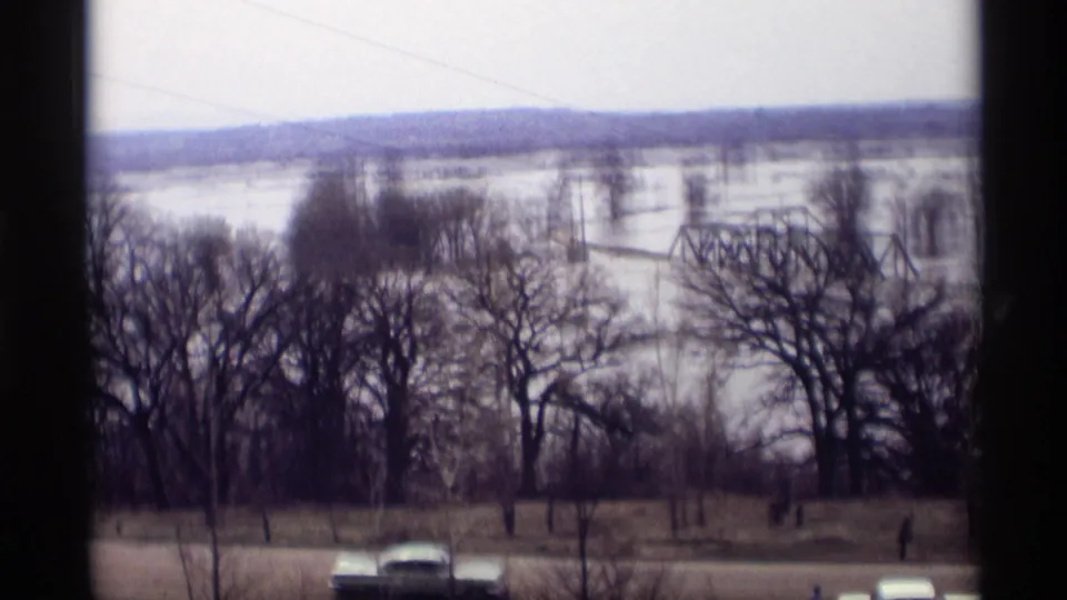Elevated 1969 Savage, Minnesota view of winter floodwater around bare trees and a steel truss bridge, with a period car on the foreground road.