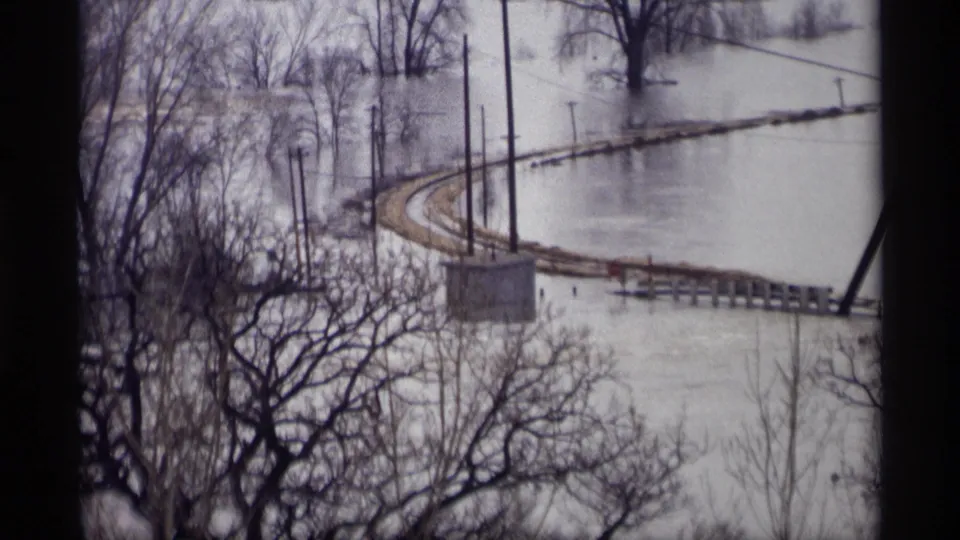 Savage, Minnesota flood scene from 1969 showing a rail curve partly surrounded by high water, utility poles, bare trees, and a dark window edge.
