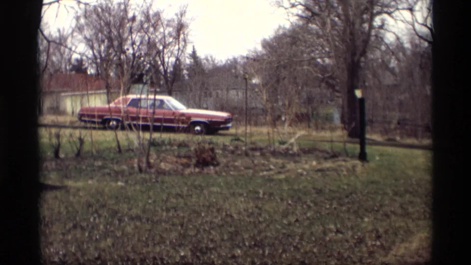 1969 Savage, Minnesota yard view with a red period car parked near bare trees, fencing, a small building, and winter-brown grass.
