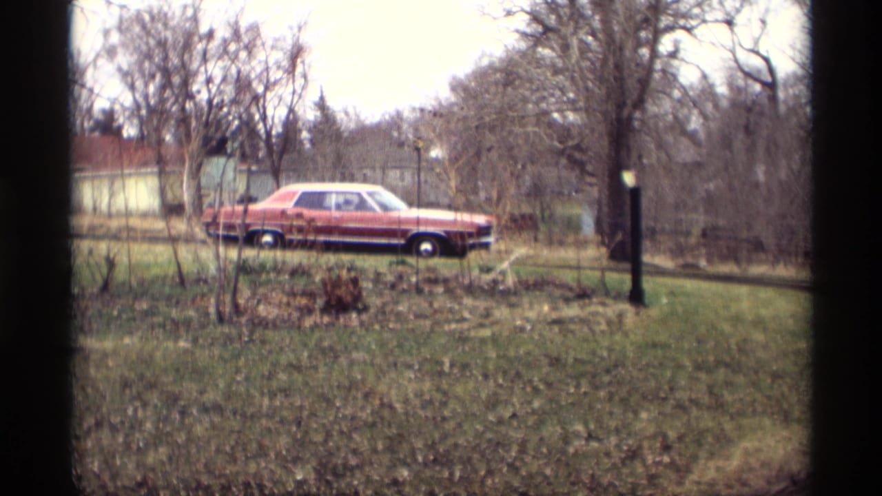 1969 Savage, Minnesota 8mm frame showing a red sedan with a light roof moving past grass, bare trees, and a dark roadside post.