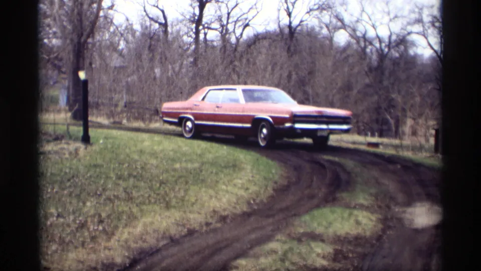 Final 1969 Savage, Minnesota frame shows the red sedan continuing around the muddy bend, with grass, posts, and bare trees visible.