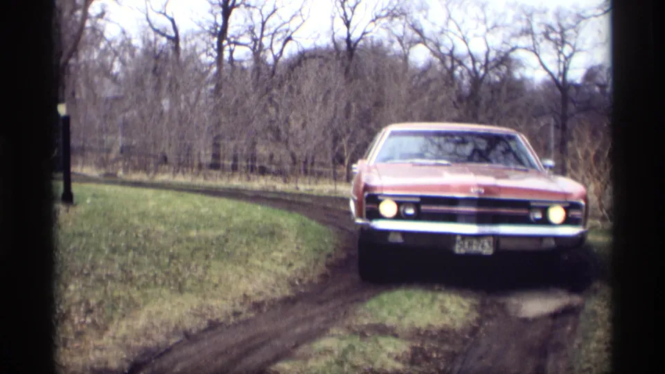 A front-facing view shows the red sedan with headlights on, chrome bumper visible, approaching on the muddy Minnesota driveway.