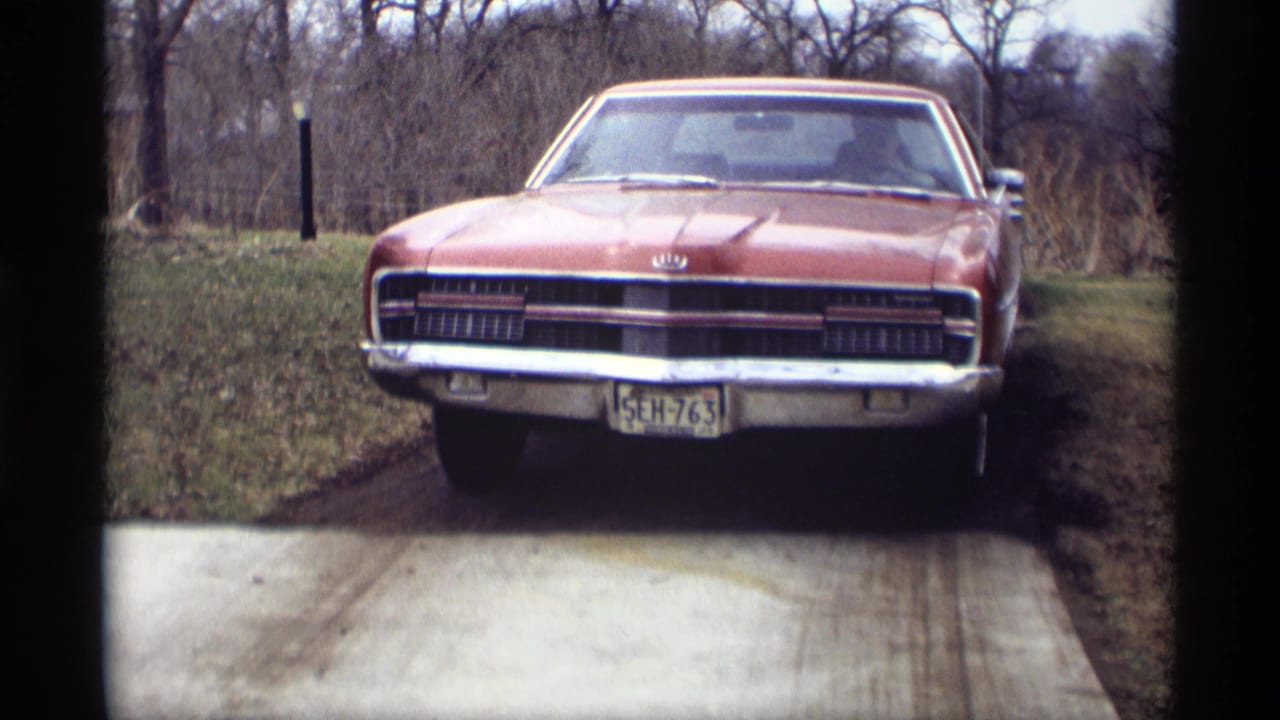 Red vintage car parked at the end of a driveway with bare trees behind it.