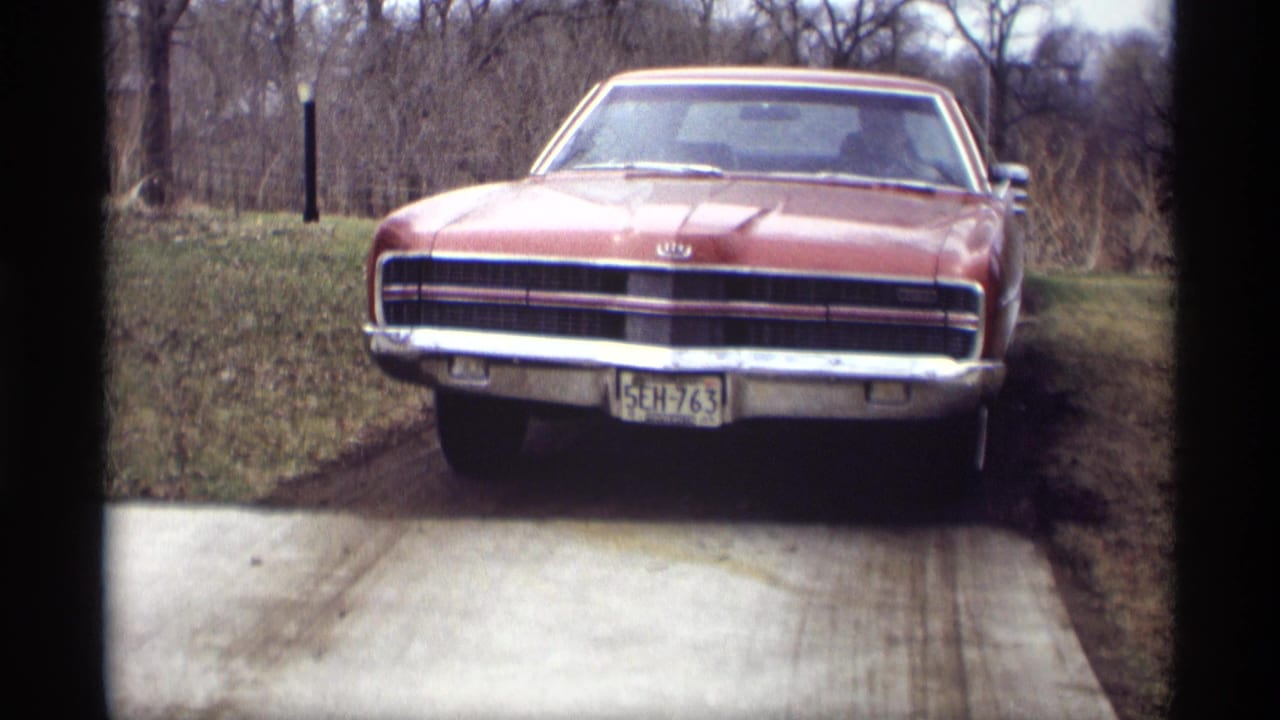 Maroon sedan facing the camera on a concrete driveway beside bare trees.