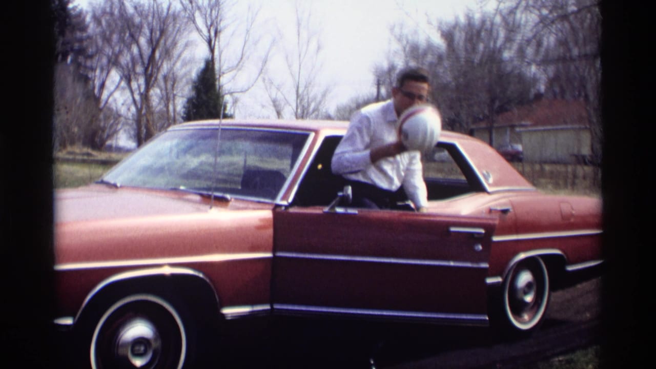 Adult man steps out of the sedan while holding a white hard hat near the open door.